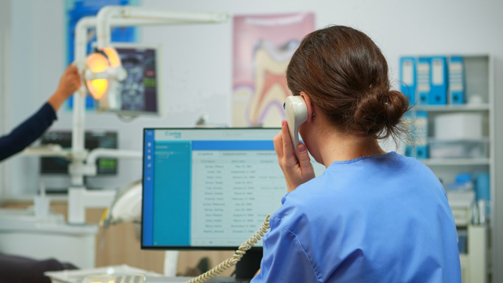 Dentist's assistant on a phone call while viewing booking information on a computer