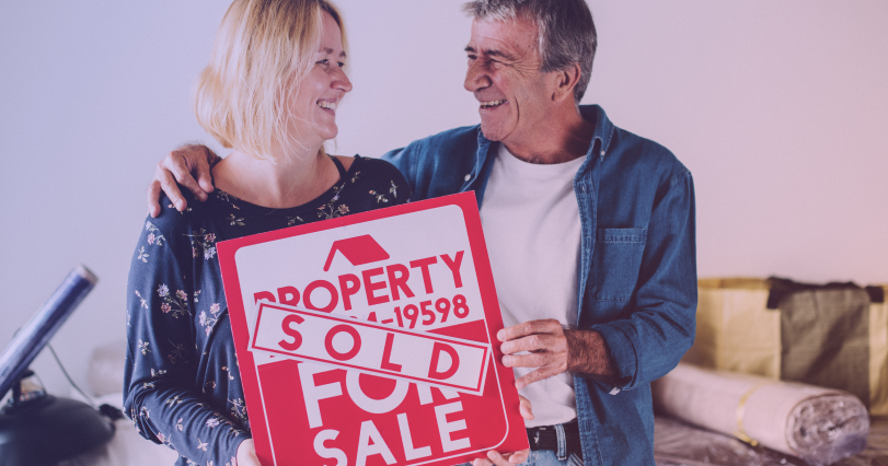 couple standing together with sold property sign